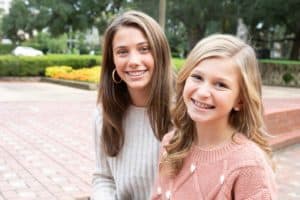 Girl with brown hair and younger girl with blond hair smiling in a park